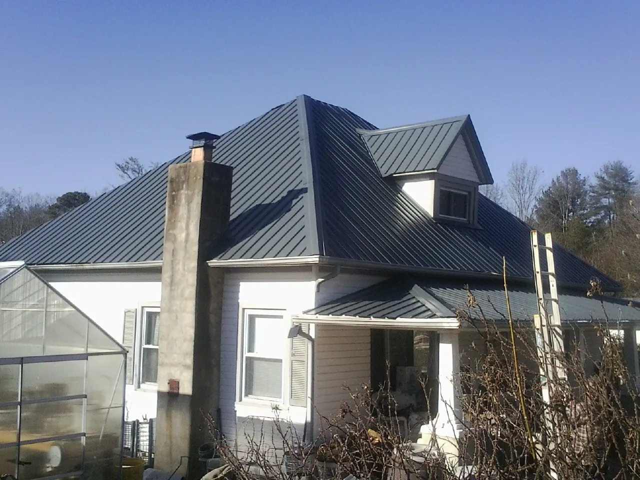 Dark blue standing seam metal roof on a white farmhouse with dormer — Slate & Tile Roof Repair by Roofing Brothers in Liscomb