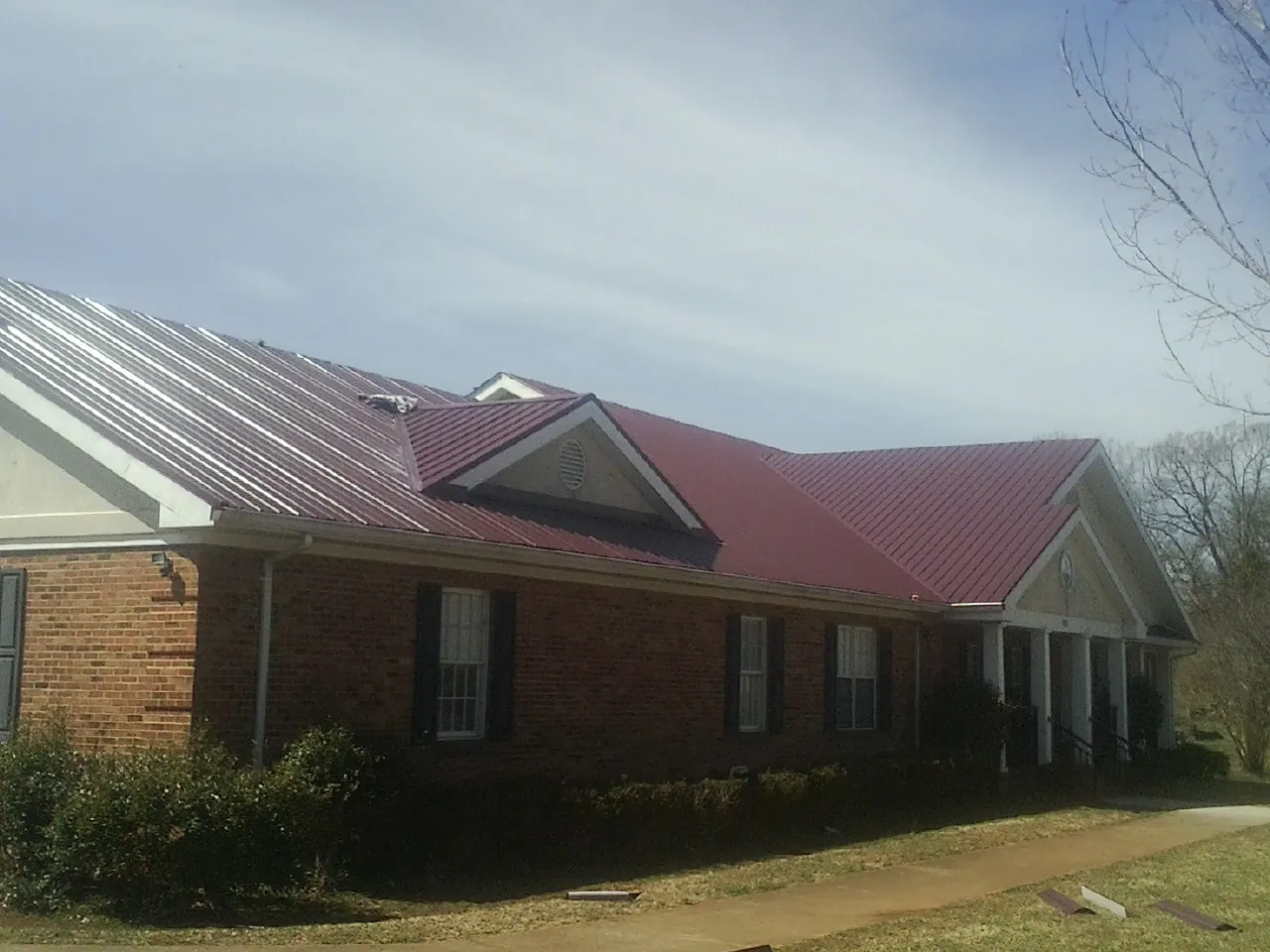 Red metal roof with gabled entries on a long brick building, from a Hail Damage Roof Repair job in Liscomb