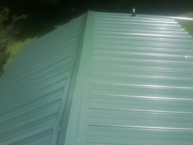 New green metal panels meeting at the ridge of a roof — Flat Roof Repair work by our crew in Liscomb