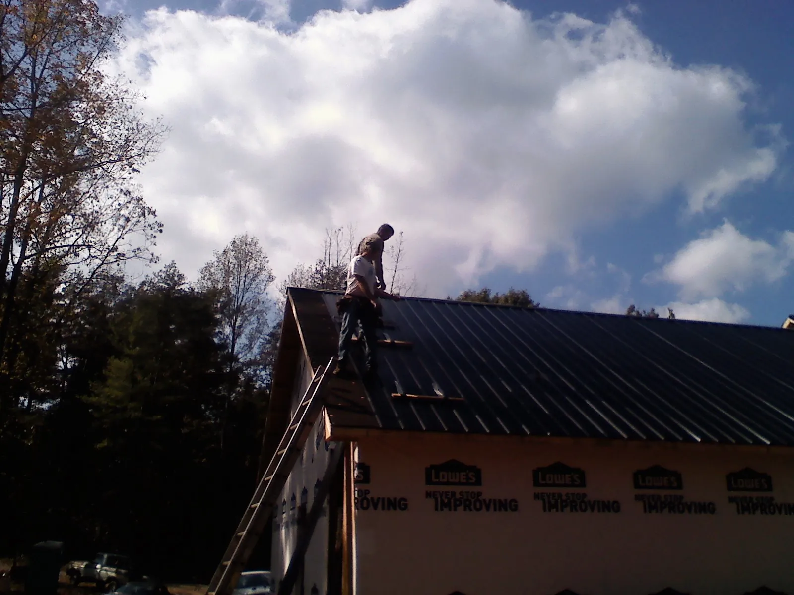 Roofer fastening dark metal panels high against a cloudy sky, from a Roof Inspection job in Liscomb