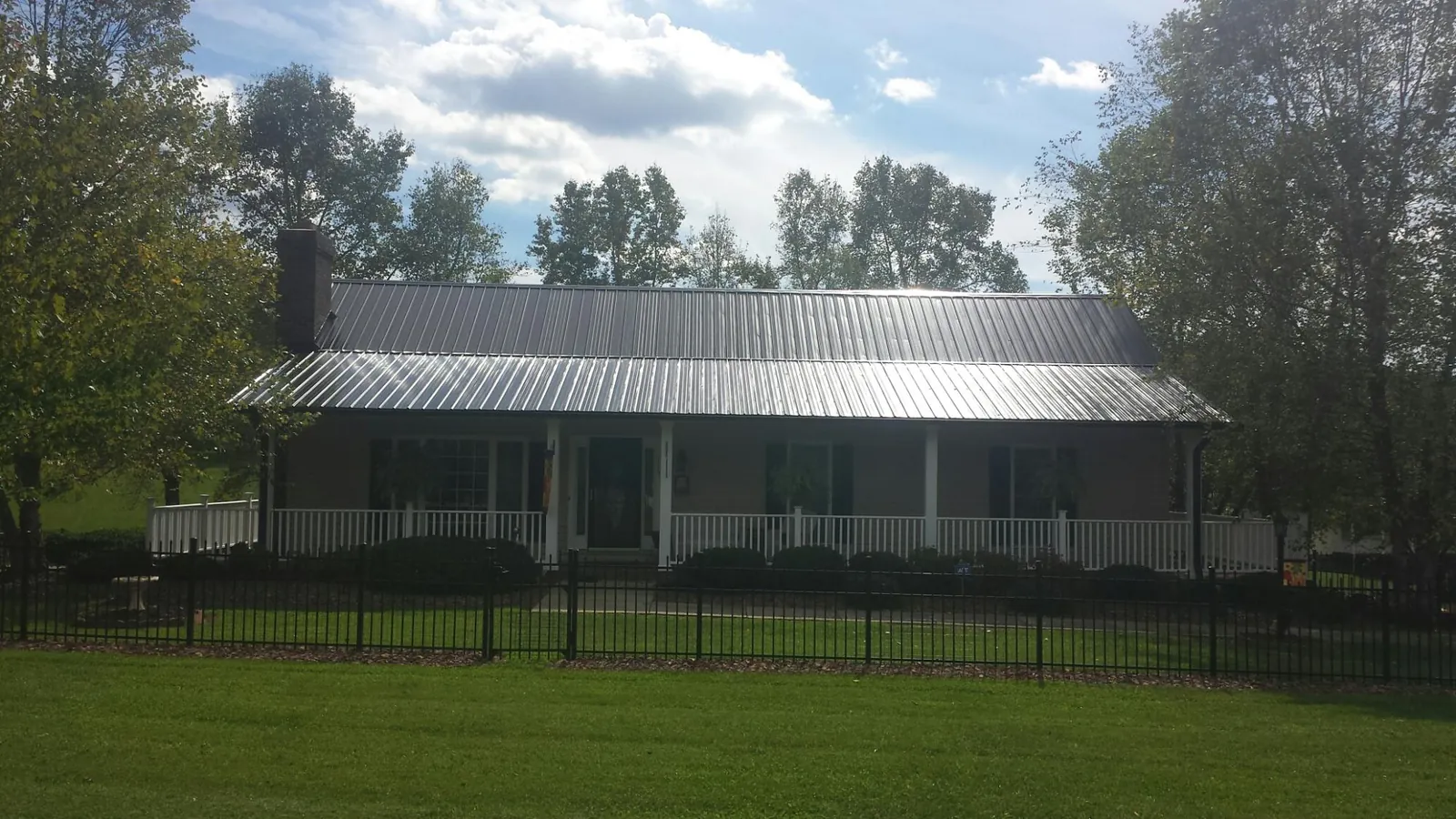 Gray metal roof on a brick ranch with a full width front porch — Gutter Guard Installation work by our crew in Liscomb