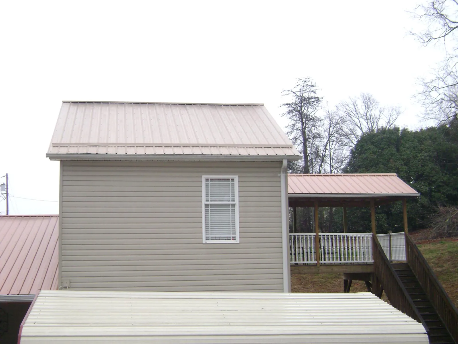 Tan metal roofs on a two story addition and attached porch, from a Roof Replacement job in Liscomb